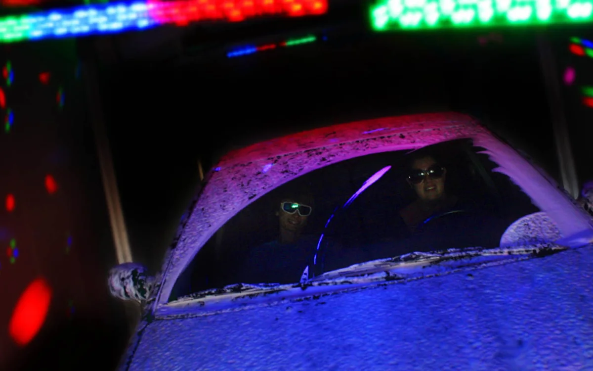 A foam-covered car under colored lights inside the Lazer Show Laser Wash